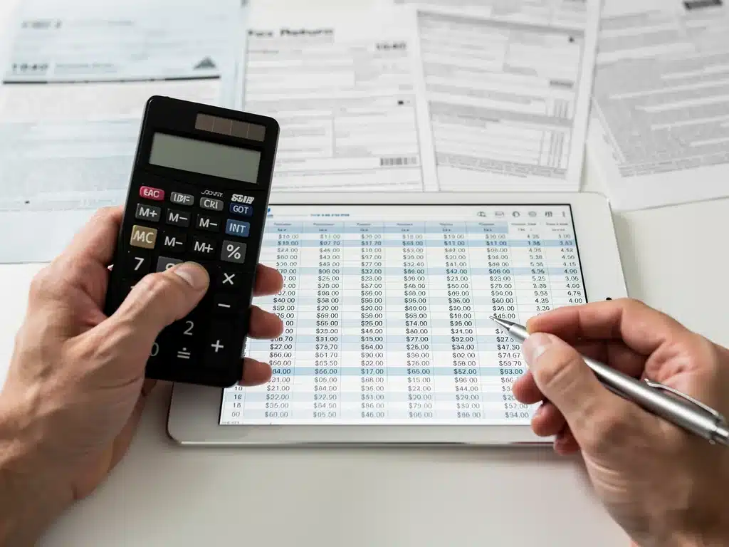 Hands calculating finances on a tablet, preparing for tax adjustments.